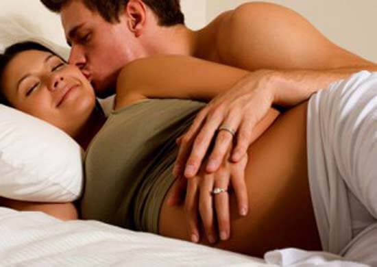 Pregnant woman and husband lying in bed smiling