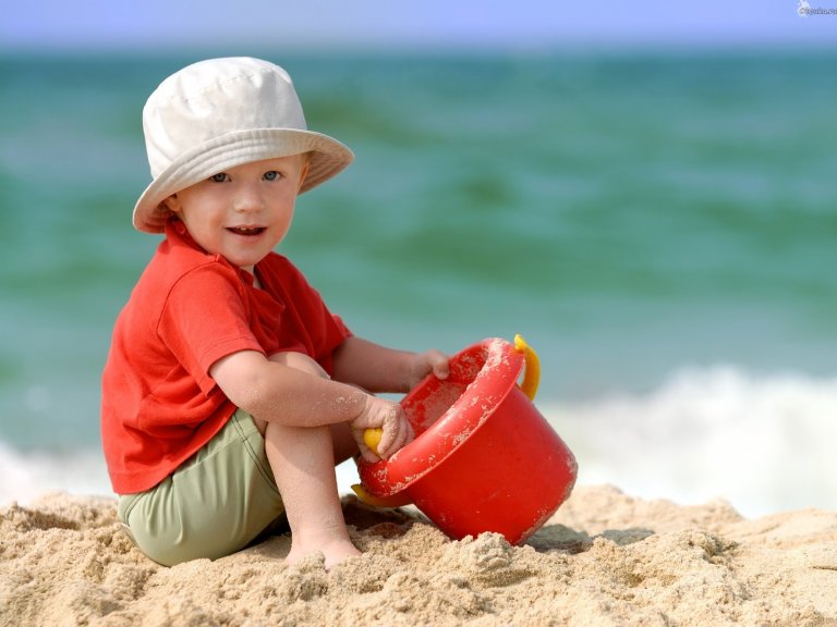 Boy playing in the sand with white hat