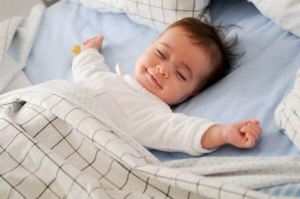 baby smiling while sleeping in large bed