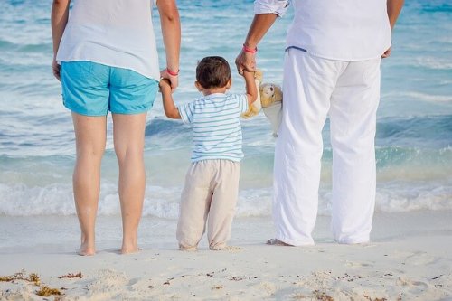 parents holding baby's hands on the beach