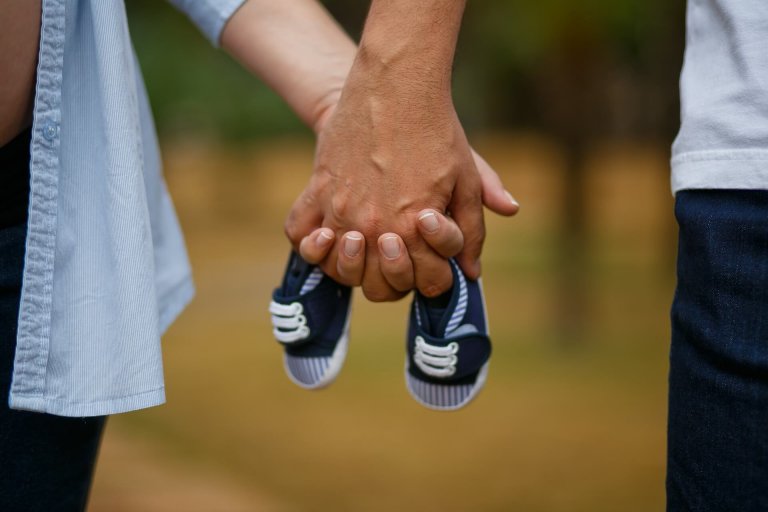 partners holding hands and baby shoes