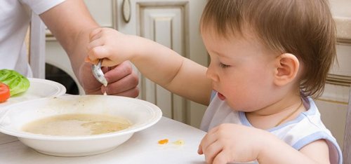 lille barn der prøver at spise suppe selv