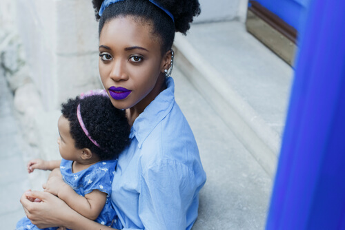 afroamerikansk mor med lilla læbestift og barn i skødet