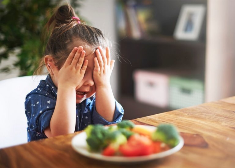 lille pige der holder sig for øjnene med tallerken foran sig med mad