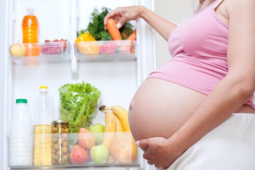 A pregnant woman grabbing fresh produce from the refrigerator.