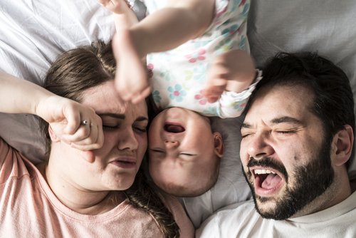 frustrerede forældre og baby i midten i en seng