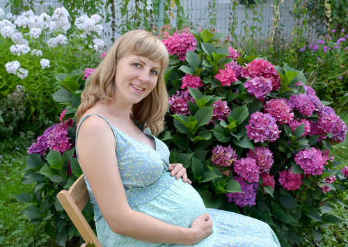 gravid kvinde på træstol foran blomsterbusk