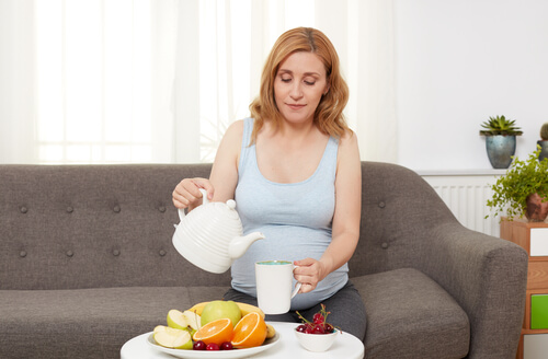 kvinde der hælder te op med en stor frugttallerken foran sig