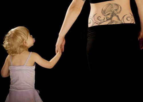 mor med tatovering på lænden der holder datter i hånden