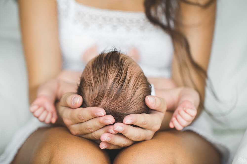 A mother holding her newborn's head in her hands while he lies on her lap.