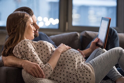 mand og gravid kvinde der ligger i sofa med tablet