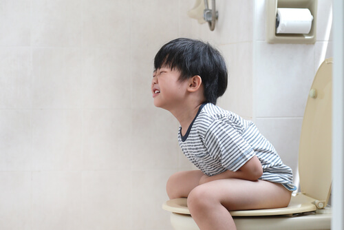En liten asiatisk pojke som sitter på en toalett förstoppning.