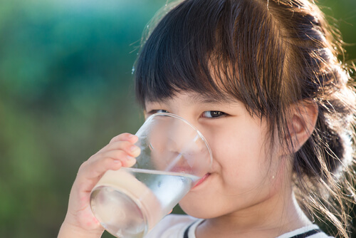 A small Asian girl drinking a glass of water.