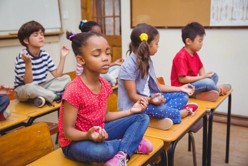 børn i klasseværelse der sidder på bordene og mediterer