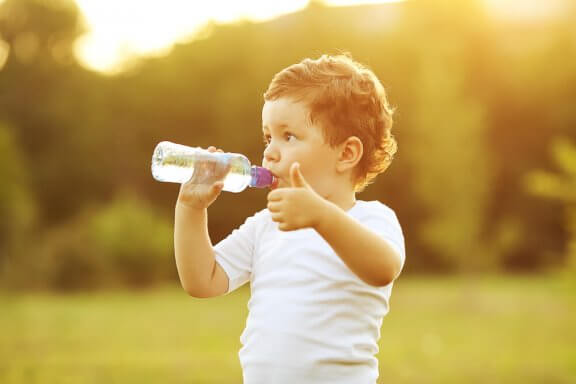 A toddler drinking a bottle of water and giving a thumbs up.