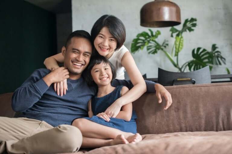 An Asian family with an only child sitting on a couch and smiling.