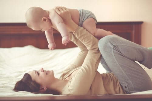 A mother playing with her baby on the bed.