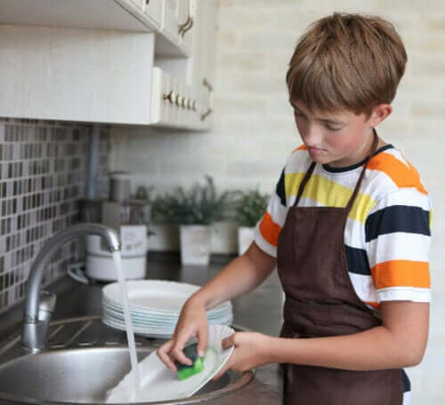 A young boy washing the dishes.