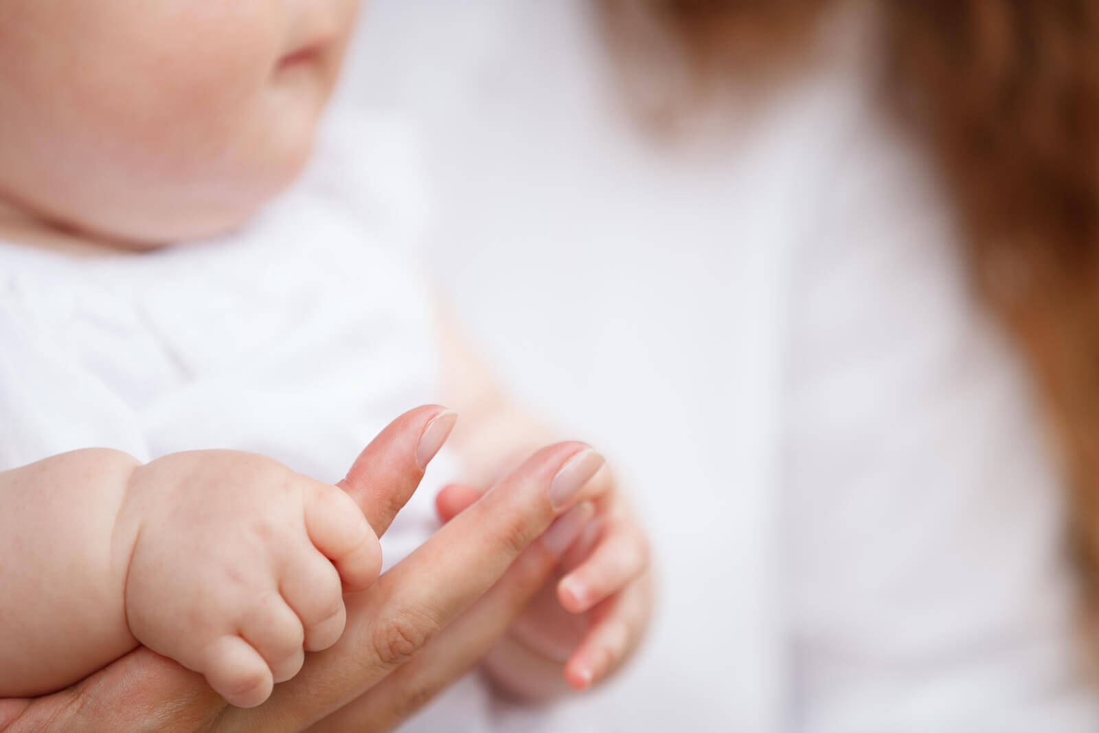 A baby holding his mother's finger.