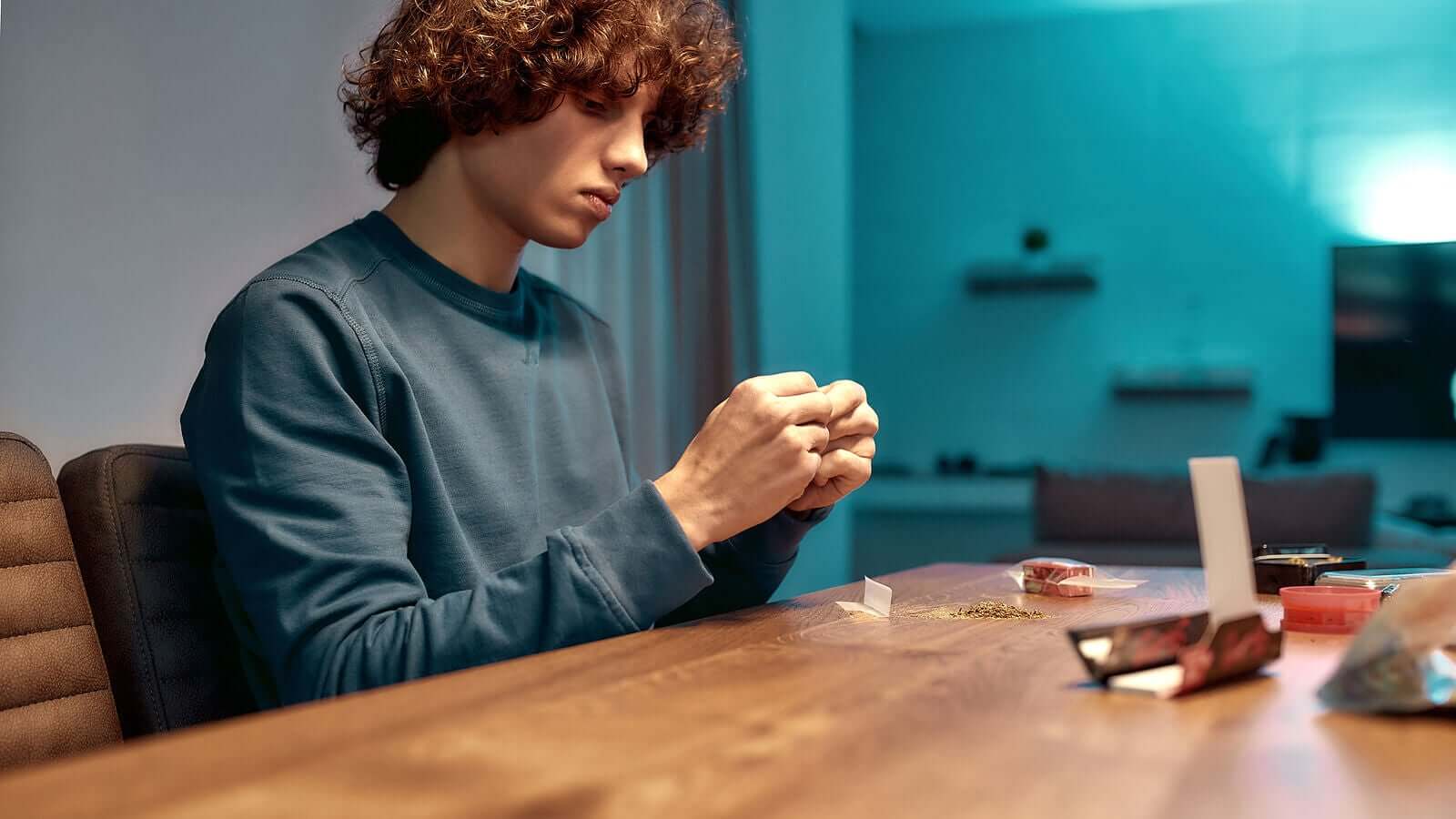 A teenage boy making a cannabis joint.