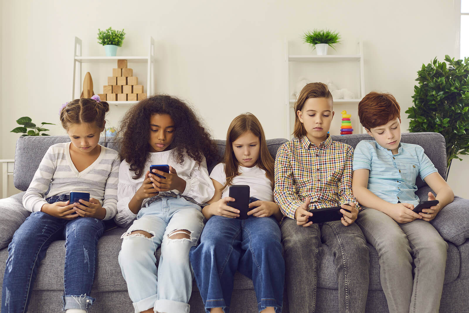 Five preteens sitting on the couch looking at their phones.
