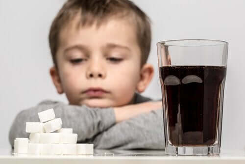 A small child staring at a pile of sugar cubes next to a glass of coke.