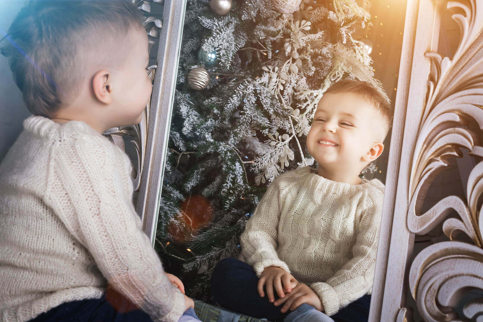 A child sitting on the floor and smilking at himself in a large mirror.