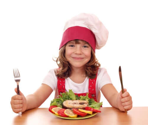 A smiling child sitting in front of a plate of fish and vegetables.