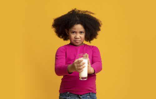 A young girl pushing away a glass of milk.