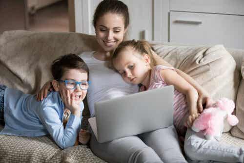 A mother looking at a laptop with her children on the couch.
