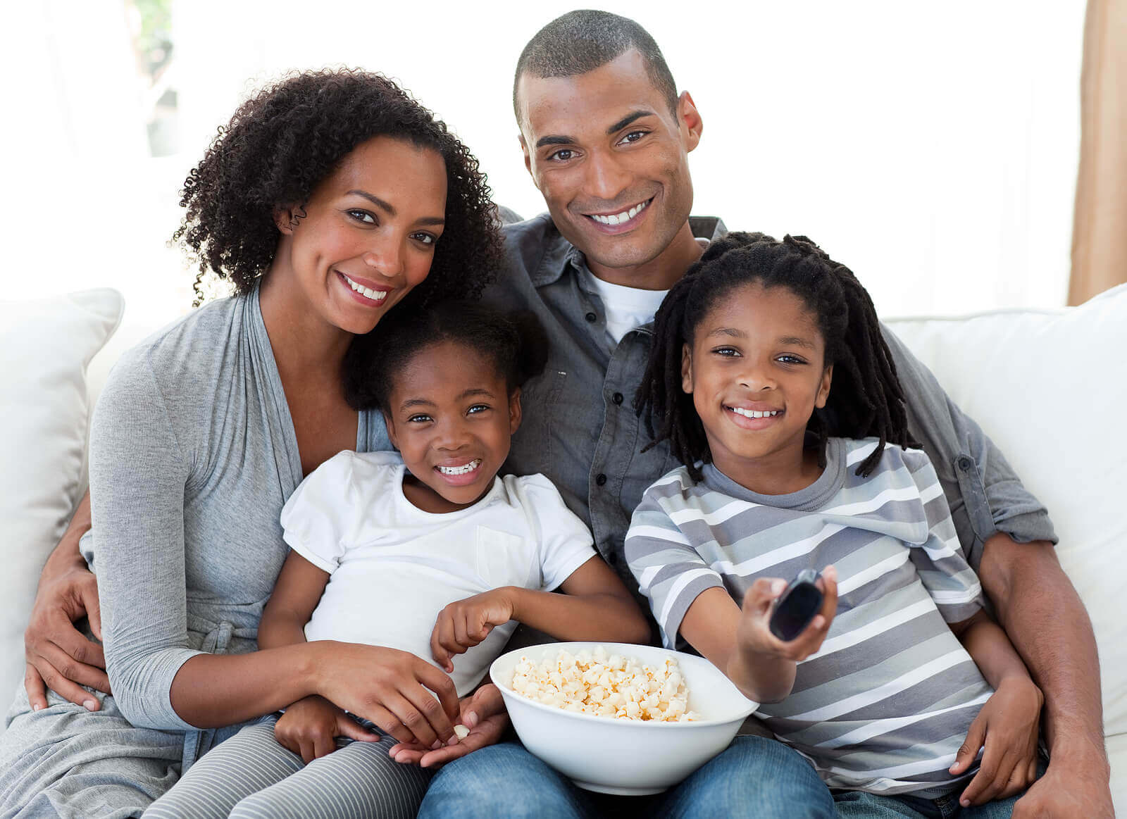 A black family sitting down with a bowl of popcorn to watch a movie.