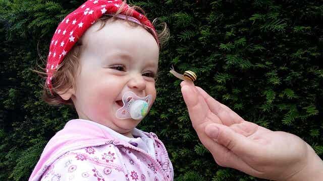 A baby girl smiling and looking at a snail.