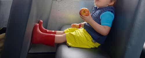 A toddler sitting on the bus eating an apple.