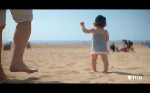 A scene from the neflix series where a baby walks on the beach.