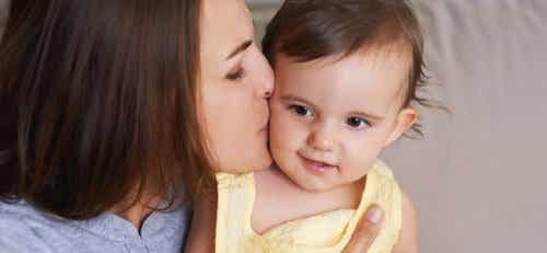 A mother kissing her baby daughter on the cheek.