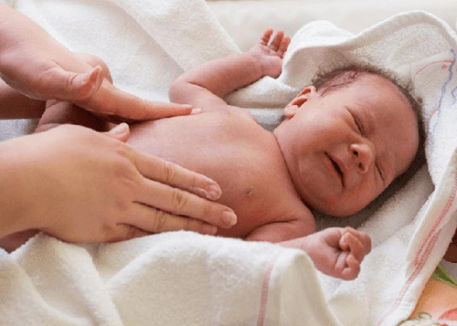 An uncomfortable newborn receiving an abdominal massage.