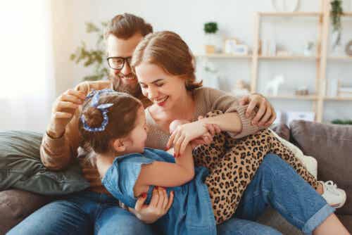 Parents playing and snuggling with their daughter on the couch.