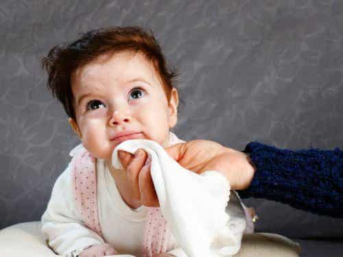 A hand wiping spit-up from a baby's mouth.