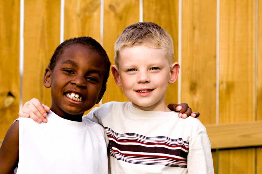 A black boy and a white boy with their arms around one another's shoulders.