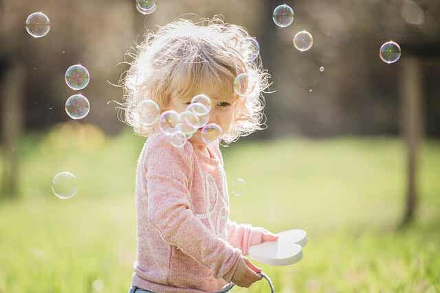 A toddler girl blowing bubbles outside.