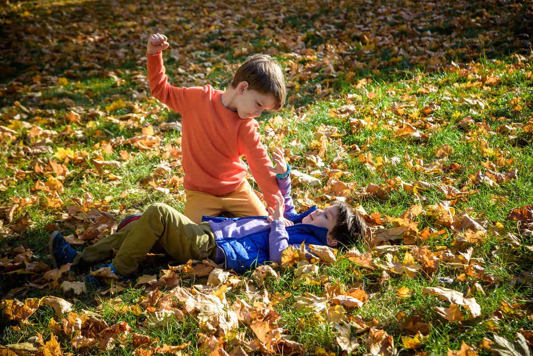 A small boy holding another boy on the ground and punching him.