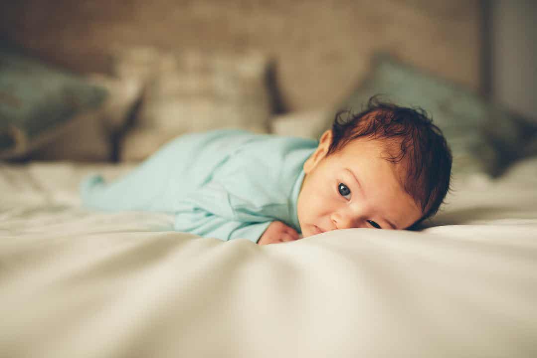 Een pasgeborene liggend op zijn buik op een bed.
