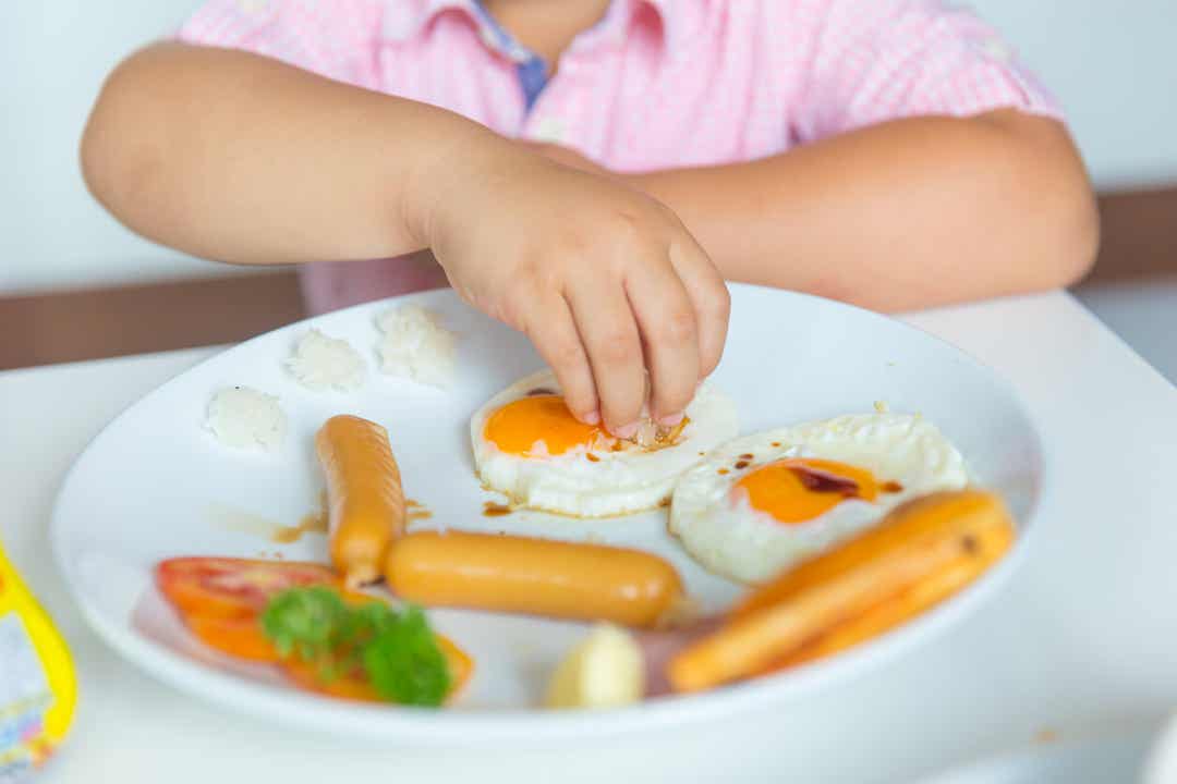 A child eating eggs and sausage links.