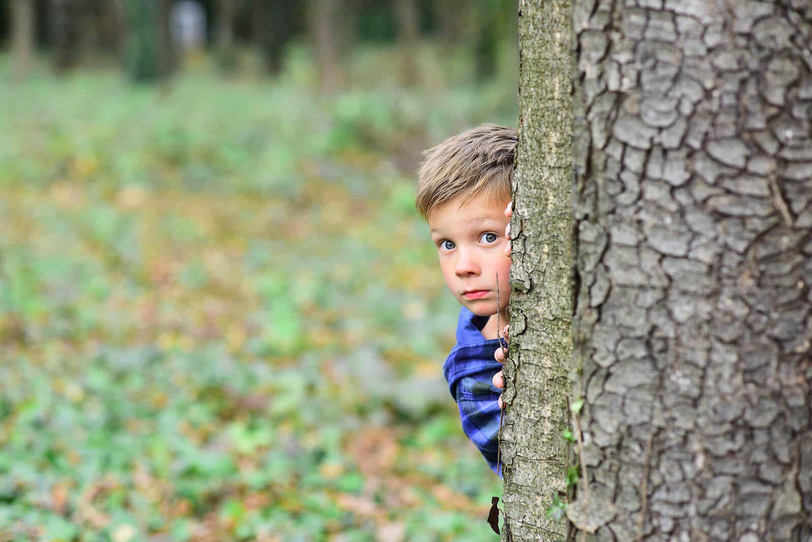 A child hiding behind a tree, looking scared.
