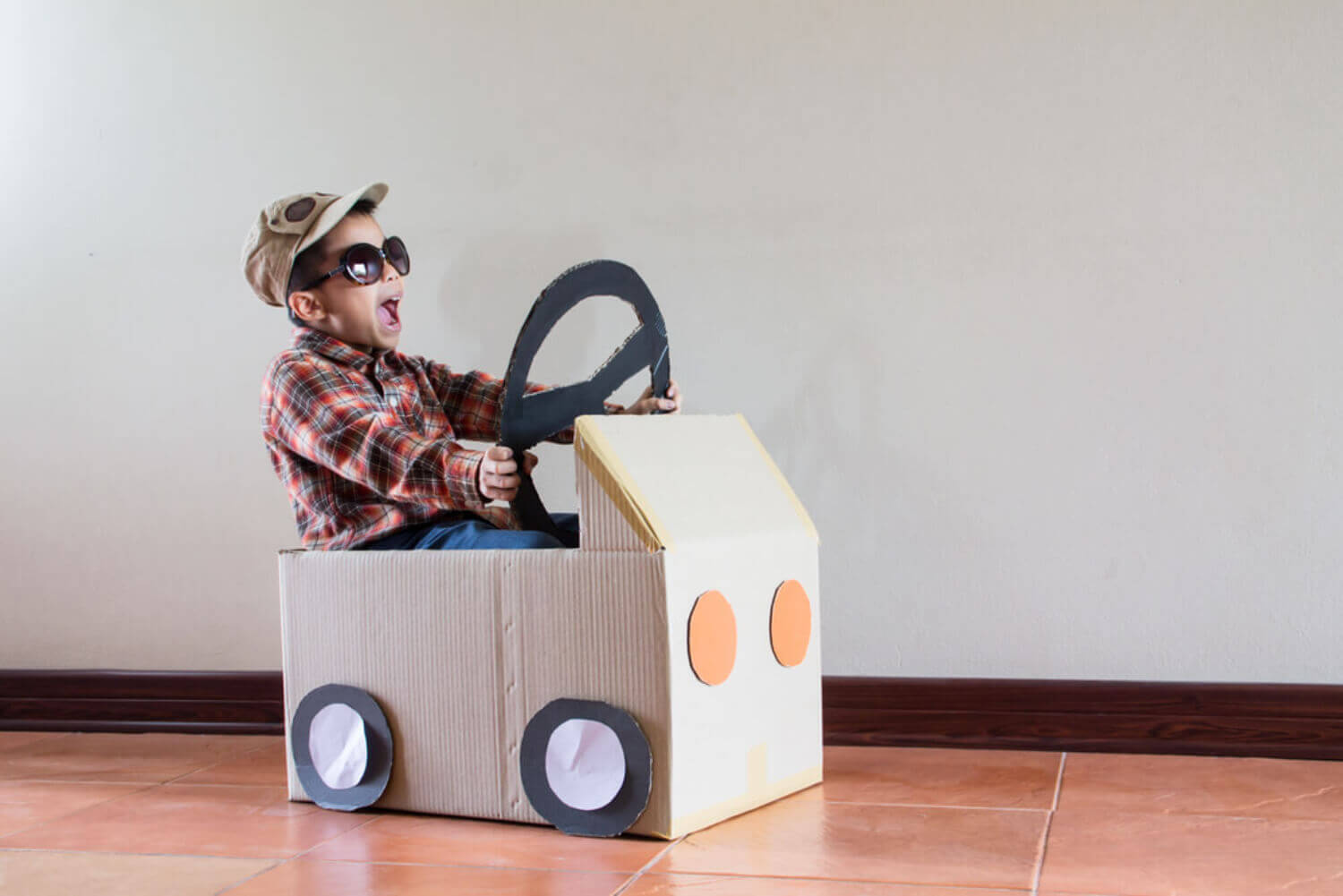 A child playing in a car made out of a cardboard box.