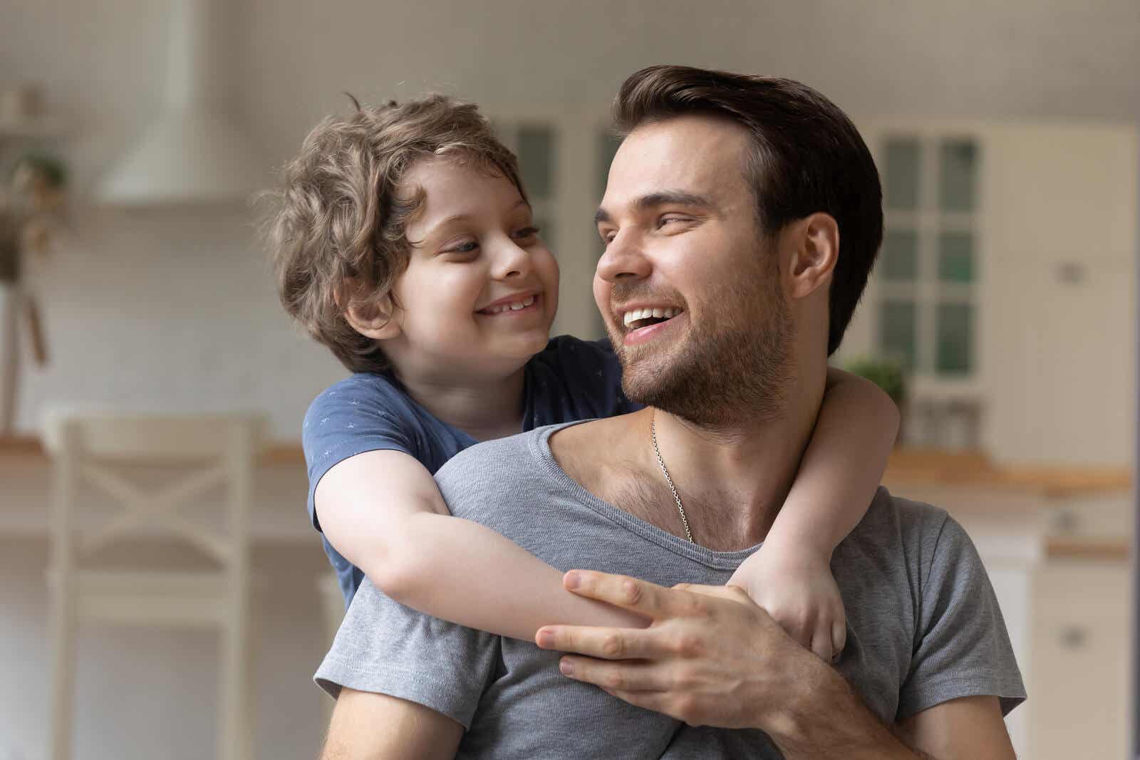 A child with his arms around his father's shoulders as they smile at one another.