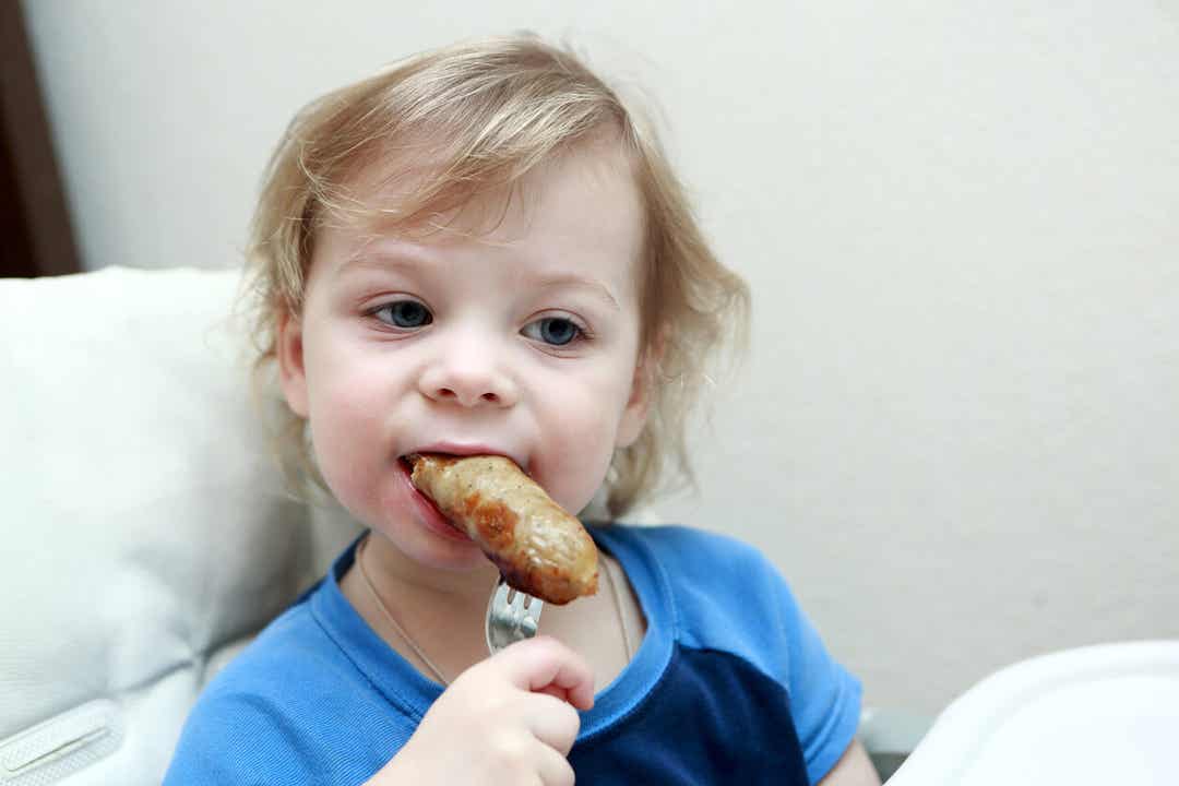 A child biting into a sausage.