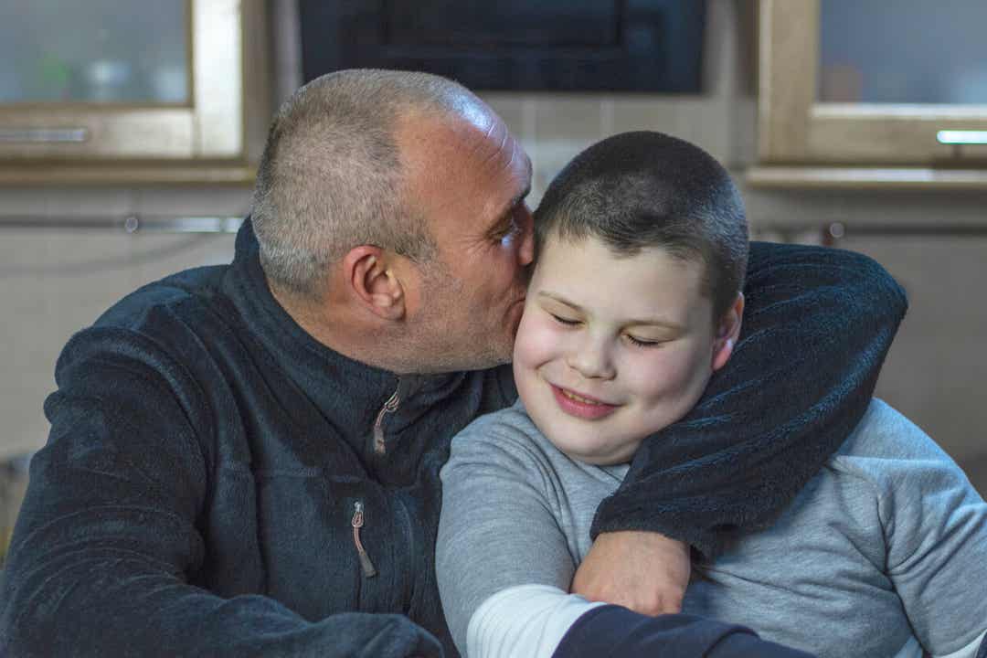 Een vader die zijn autistische zoon knuffelt en kust.
