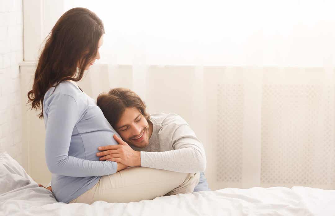 Een man die zijn hoofd op de zwangere buik van zijn partner laat rusten.