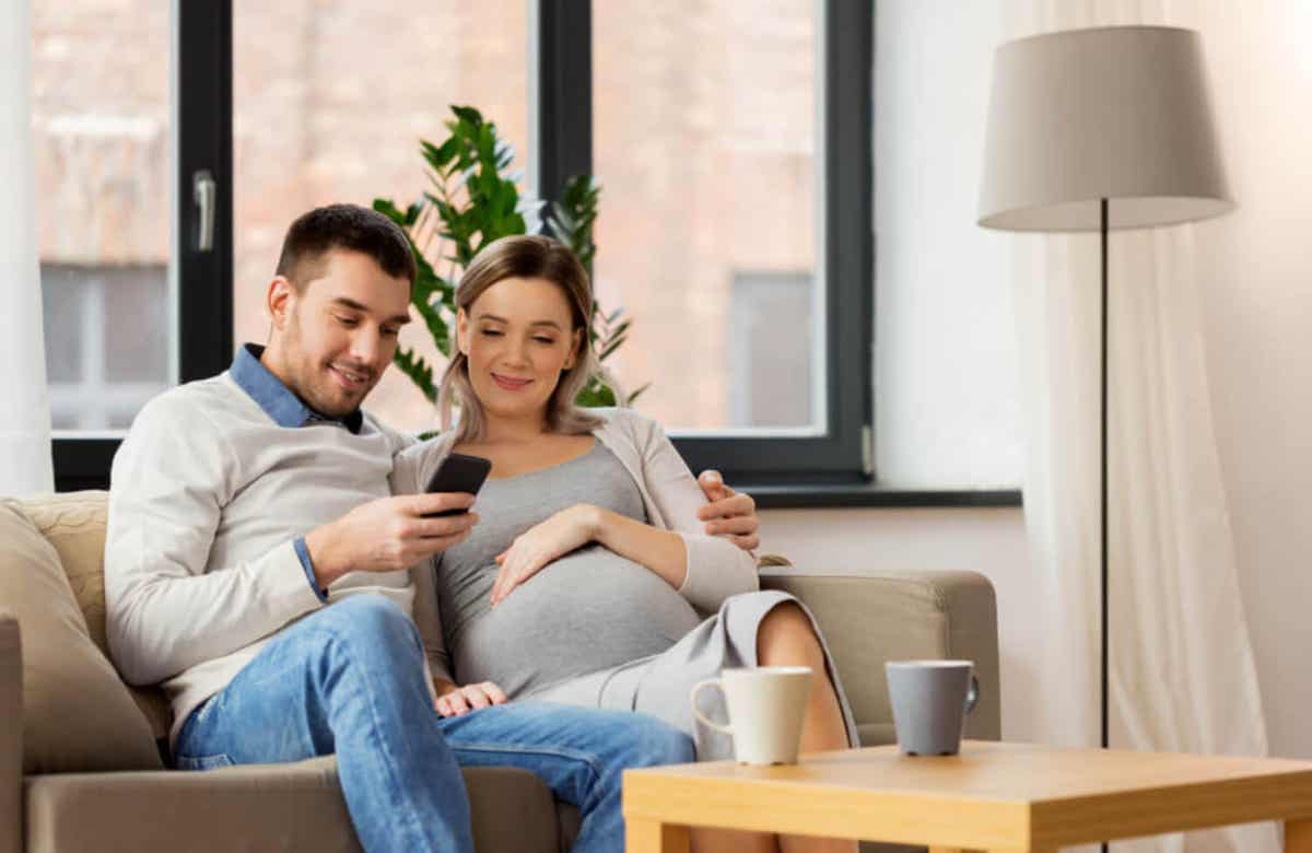 A pregnant woman and her partner looking at a cell phone and smiling.